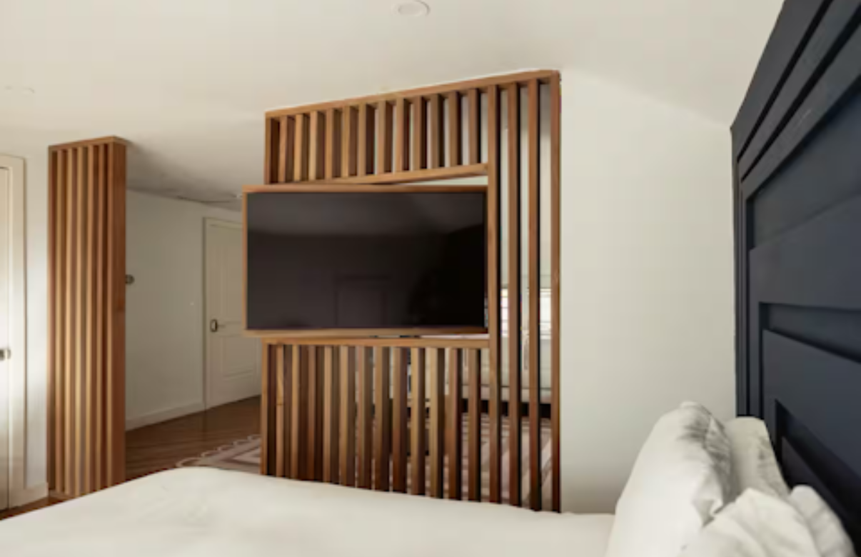 Modern bedroom with wall-mounted TV, vertical wood slats, and a bed with white bedding