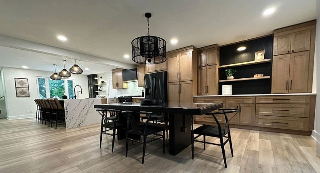 Modern kitchen with black island, wood cabinets, pendant lights, and dining area in an open-plan interior