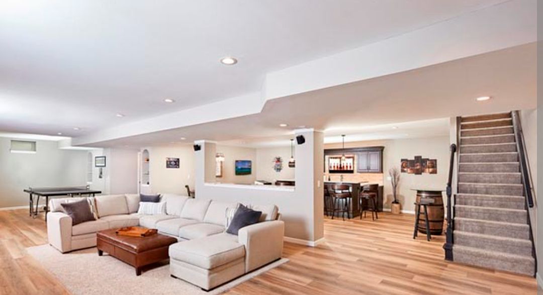 Spacious open-concept living room with gray sectional, wood floors, dining area, and staircase to the right
