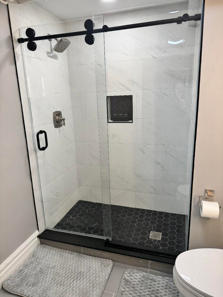 Glass walk-in shower with black trim and tiled walls in a bathroom