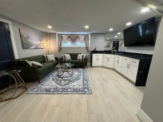 Modern living room with green sofas, patterned rug, wall art, and a large TV beside a white fireplace console