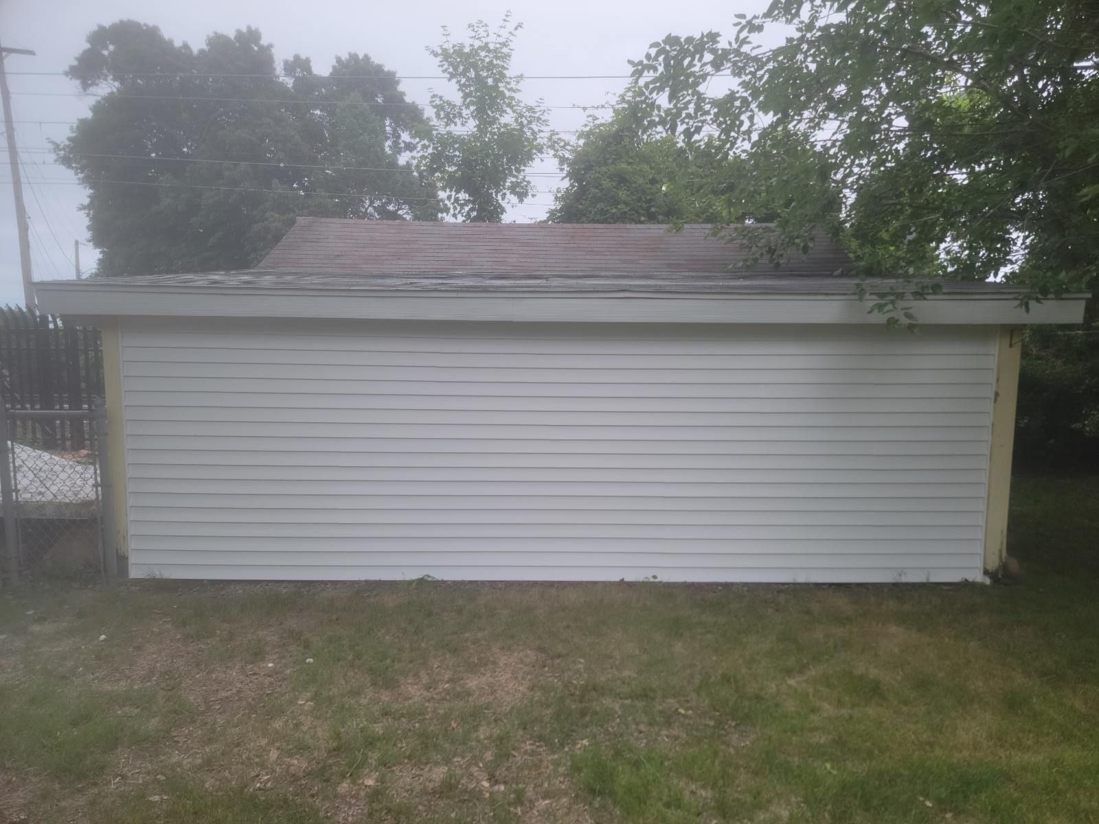 Small white detached garage with a shingled roof, surrounded by grass and trees.