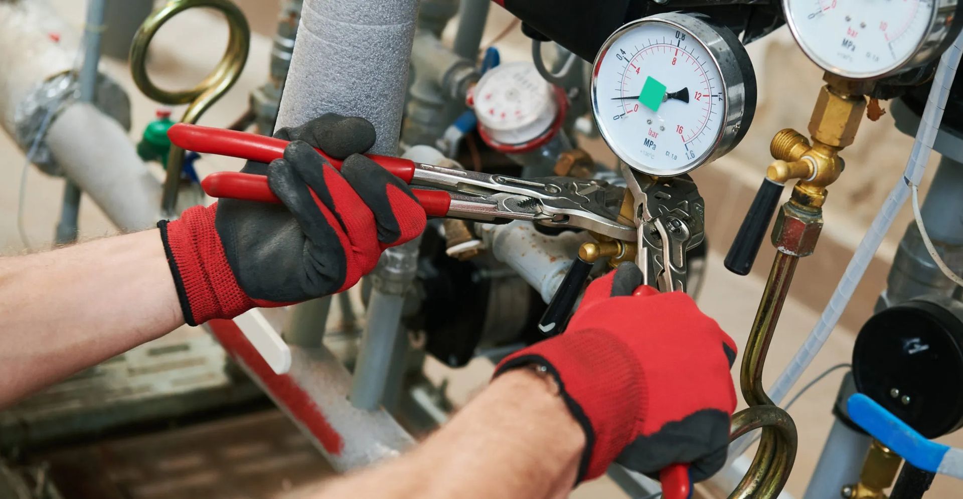 Technician adjusting hoses and gauges on industrial equipment, wearing red gloves.