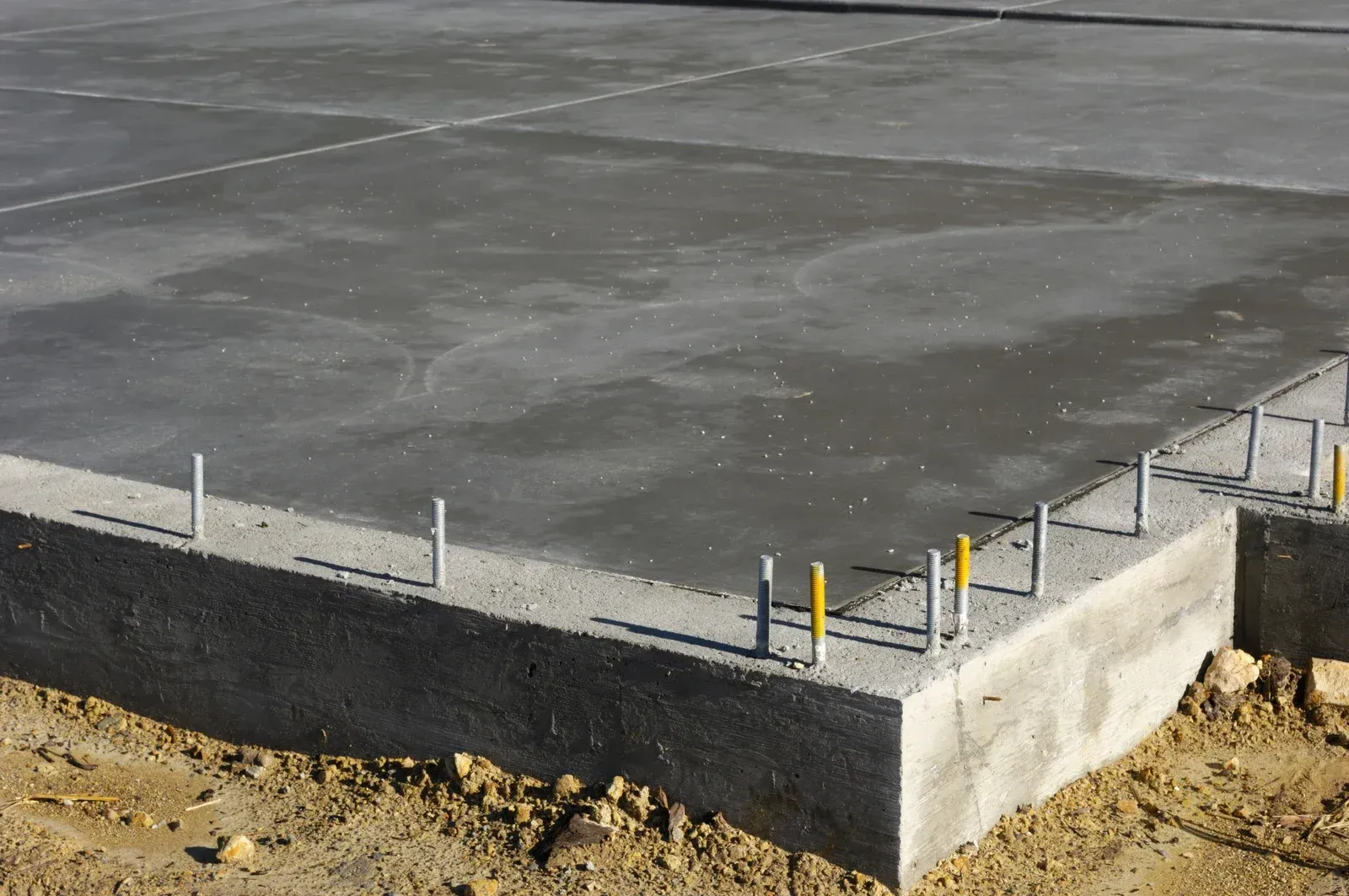 Freshly poured concrete foundation with metal rebar and yellow stakes.