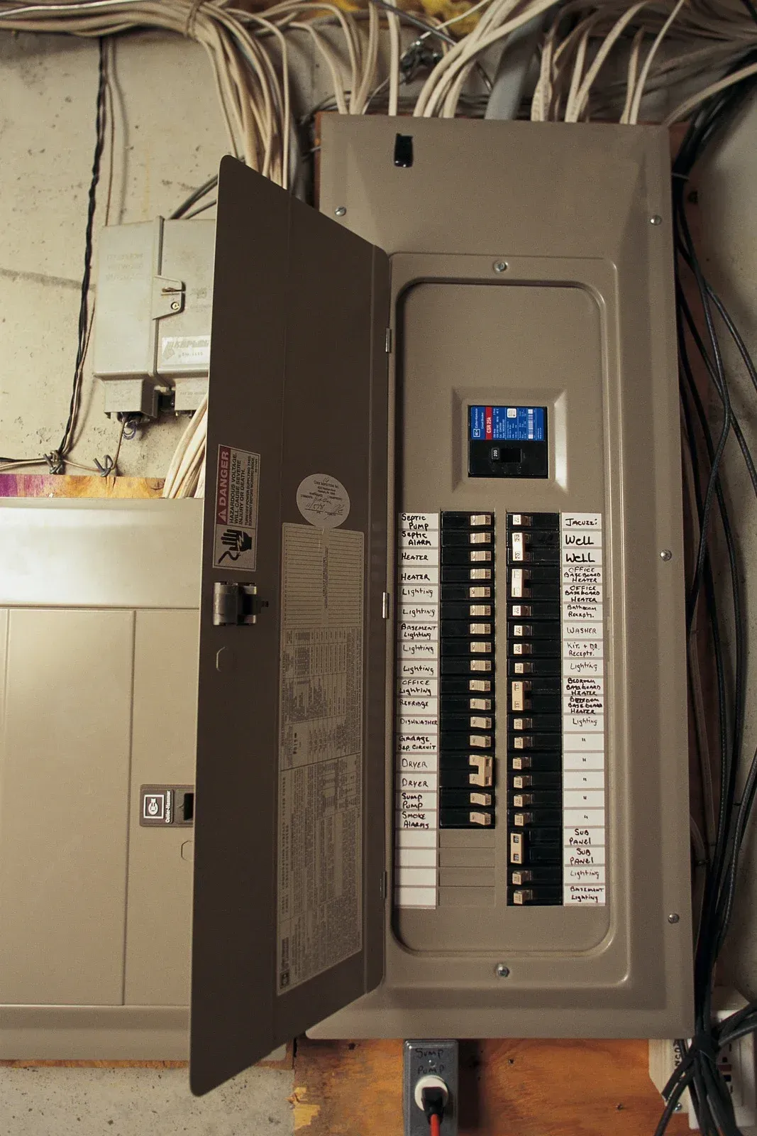 Opened electrical panel with circuit breakers. Wires and conduit visible.