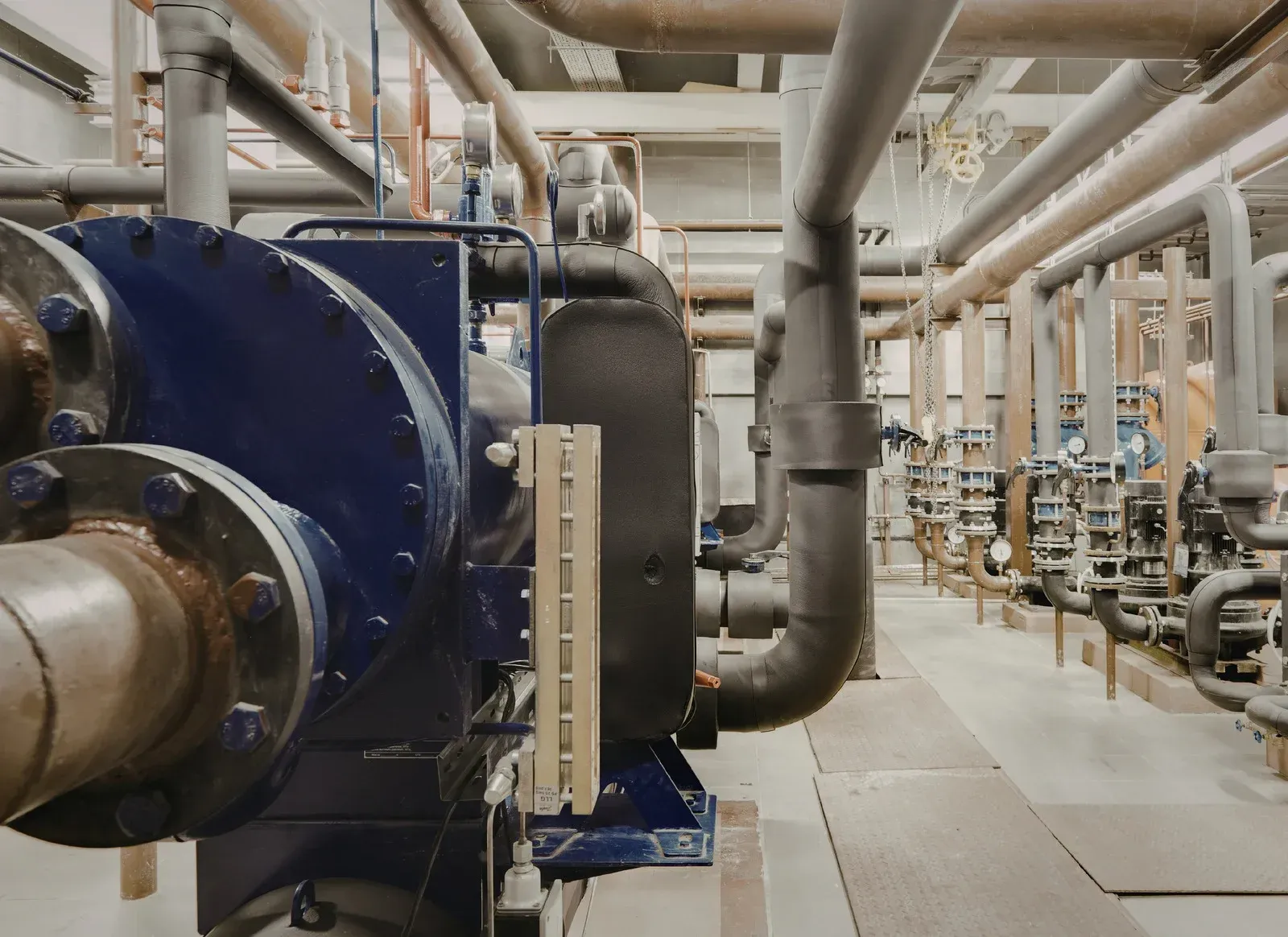 Blue industrial pump with pipes and machinery in a mechanical room.