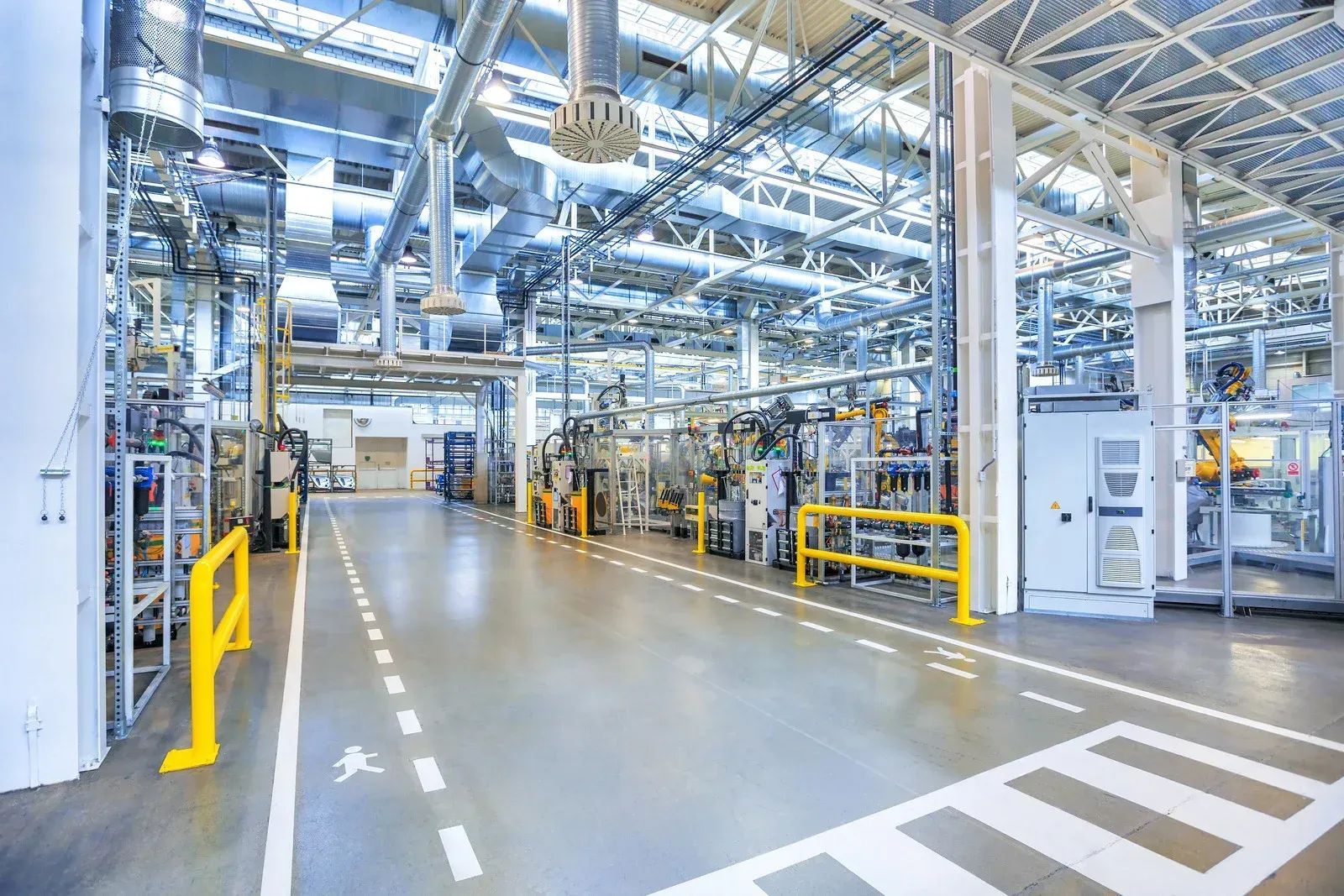 Bright modern factory interior with machinery, metal piping, and yellow safety rails along wide aisles