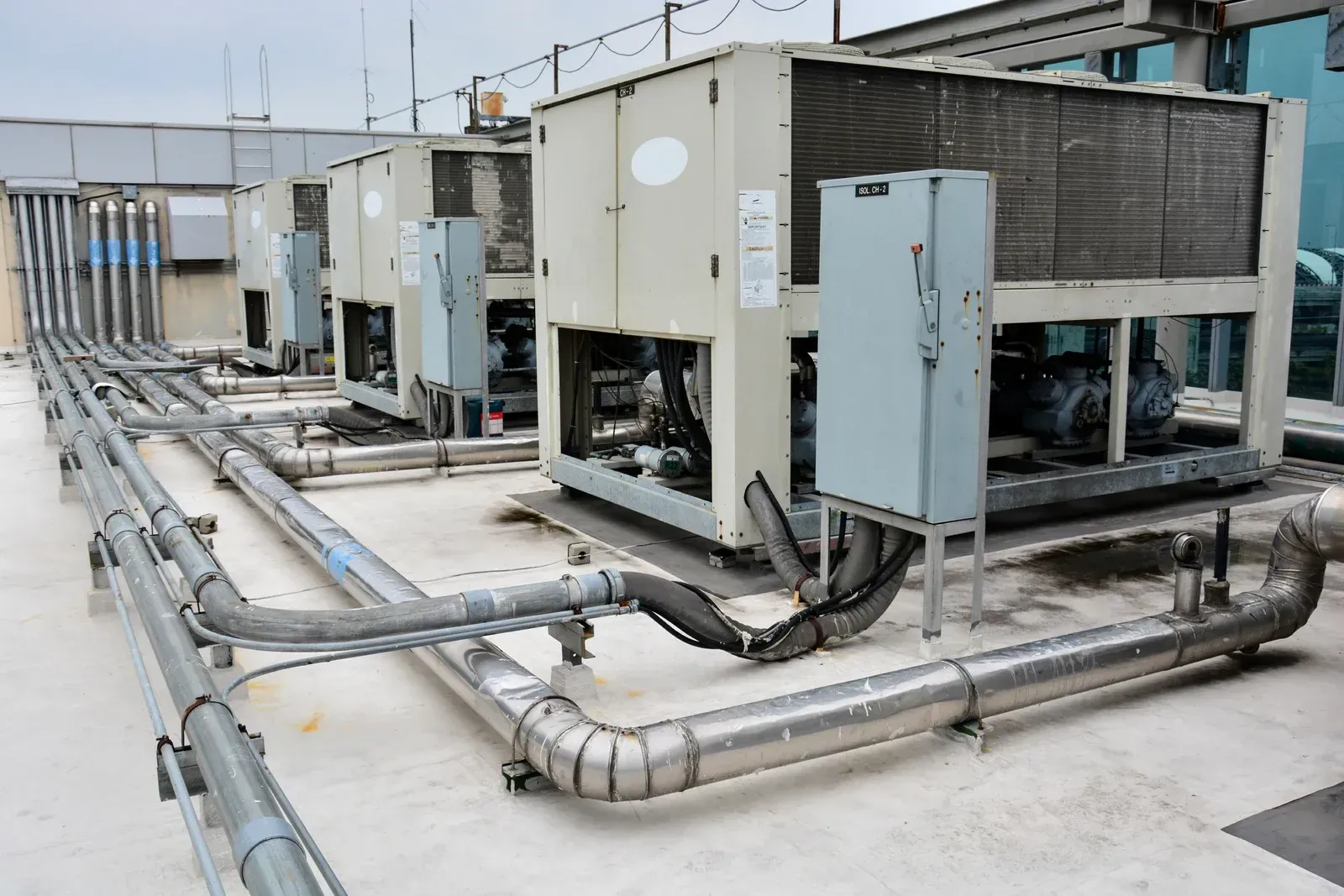Rooftop HVAC units with connected pipes. Beige equipment on a light gray surface, metallic piping.