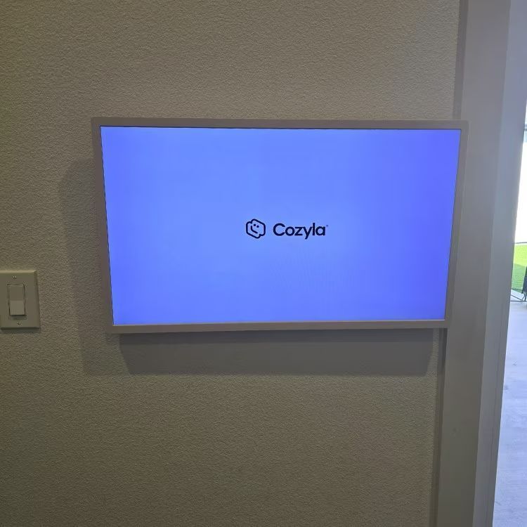 Wall-mounted screen showing the Cozyla logo on a blue background in a room
