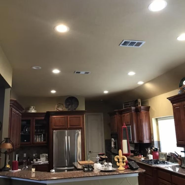 Modern kitchen with dark wood cabinets, stainless steel fridge, granite island, and recessed ceiling lights
