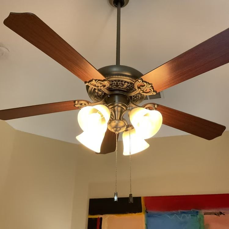 Five-blade ceiling fan with ornate bronze light fixture and frosted glass shades on a white ceiling