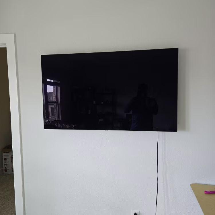 Wall-mounted black TV on a white wall with a dangling cable, next to a table edge.