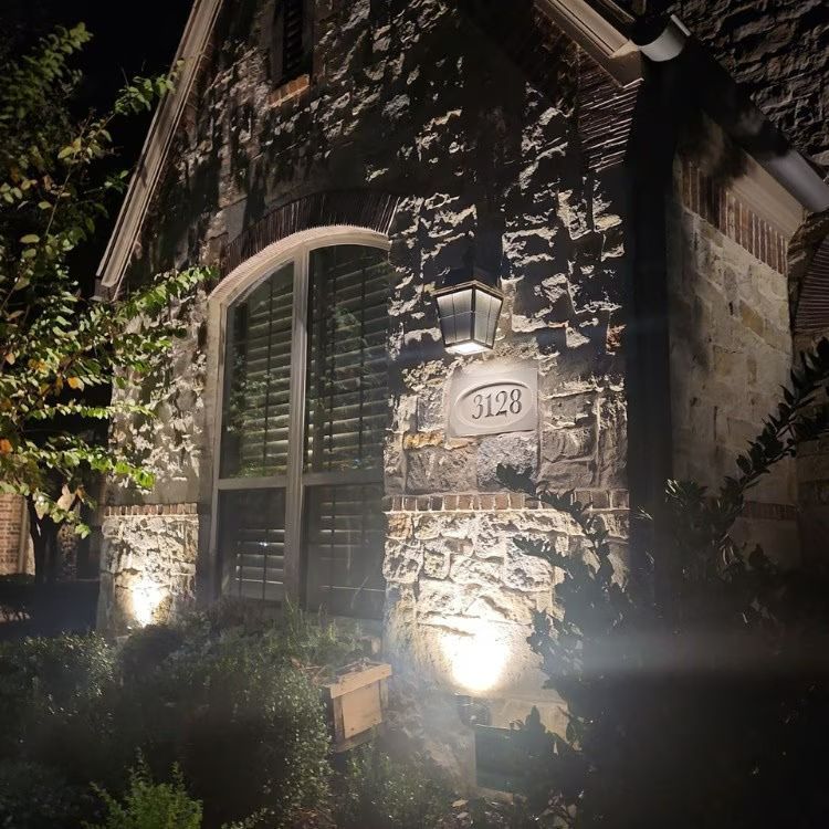 Stone house entrance at night with lit arched window, wall lantern, and house number 120