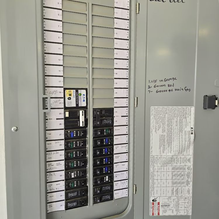 Electrical panel with labeled circuit breakers and handwritten notes on the side in a utility room