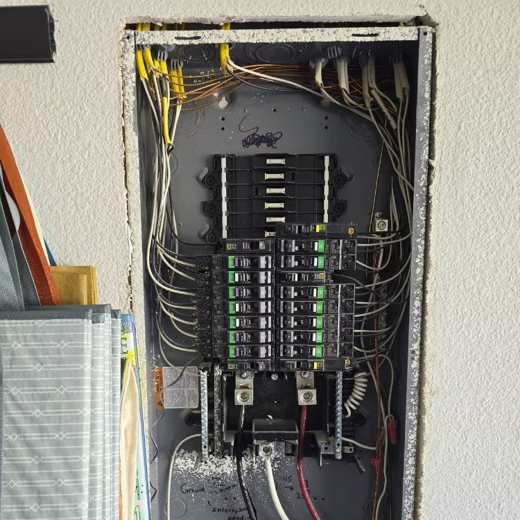 Open electrical breaker panel with many wires and breakers inside a wall recess