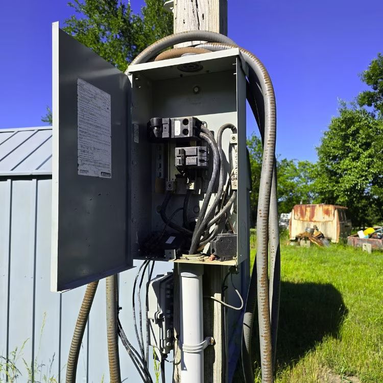 Open electrical control panel mounted outdoors with exposed wiring and conduit
