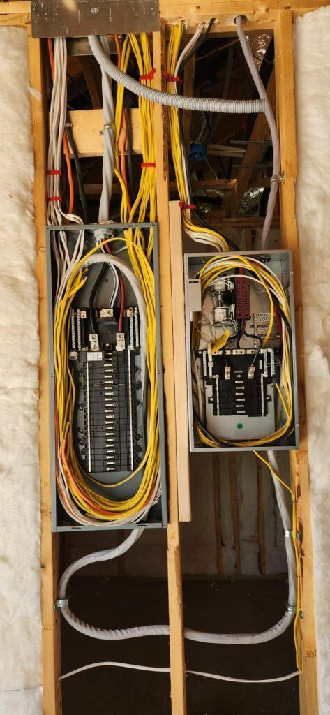 Exposed wall wiring with two electrical breaker panels and cables inside unfinished framing