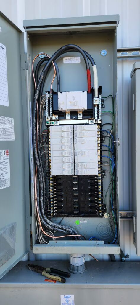 Open electrical panel with wiring, circuit breakers, and components inside a gray metal cabinet