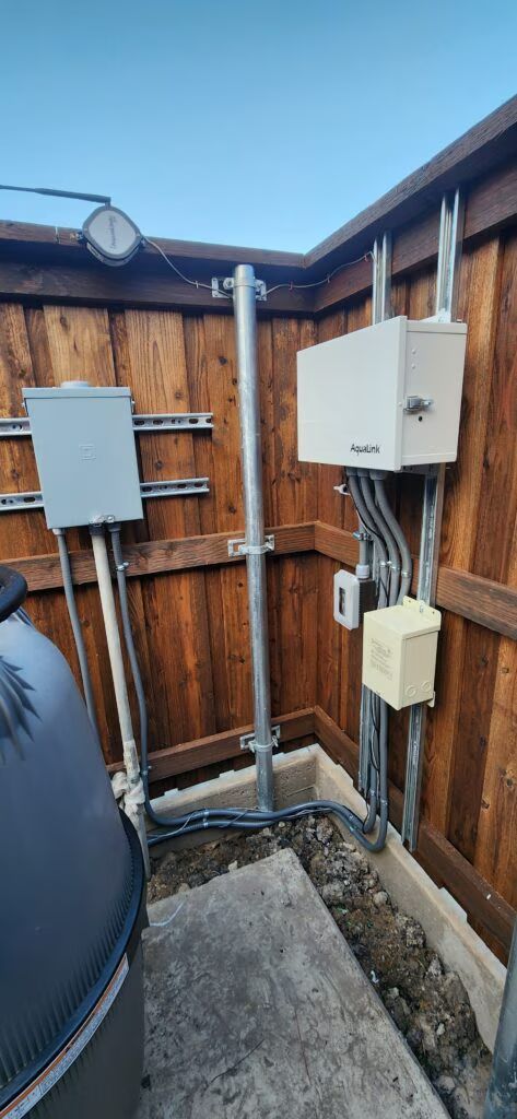 Small fenced utility area with electrical boxes, conduit, and a concrete floor.