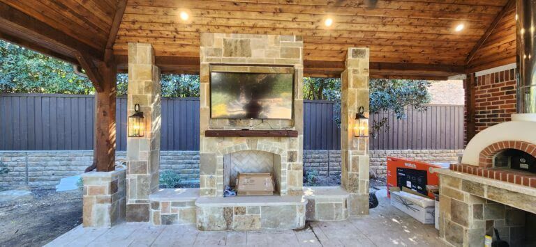 Covered outdoor patio with stone fireplace, wooden ceiling, and built-in grill area