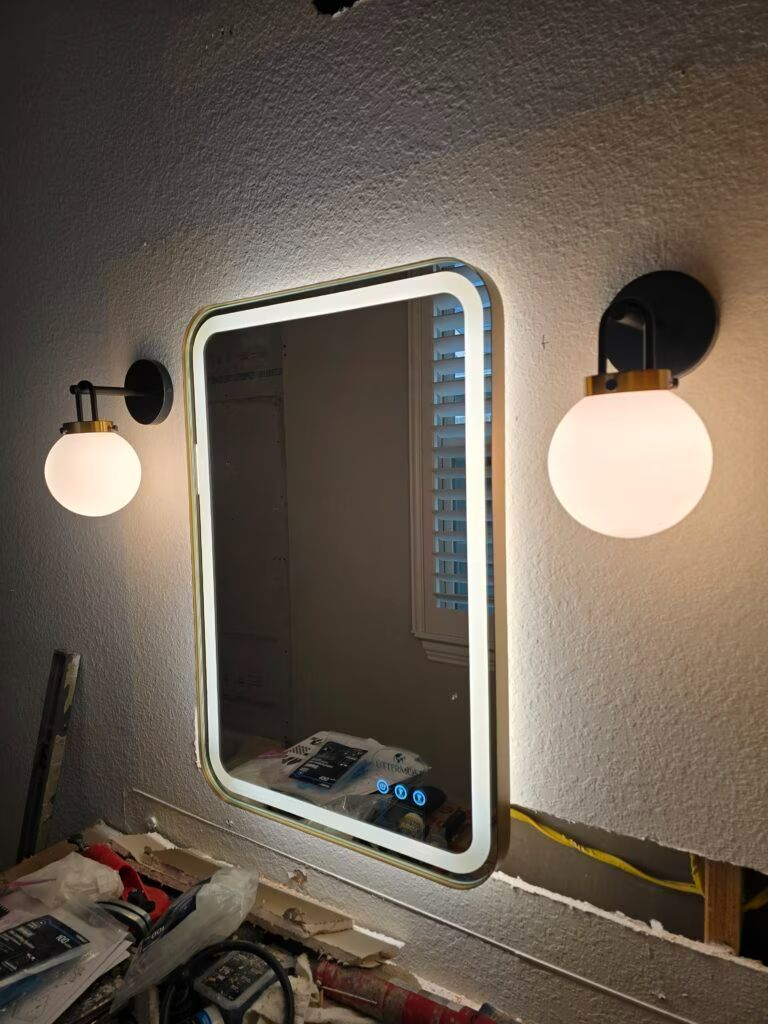 Bathroom mirror with black-and-white wall lights and a countertop cluttered with toiletries