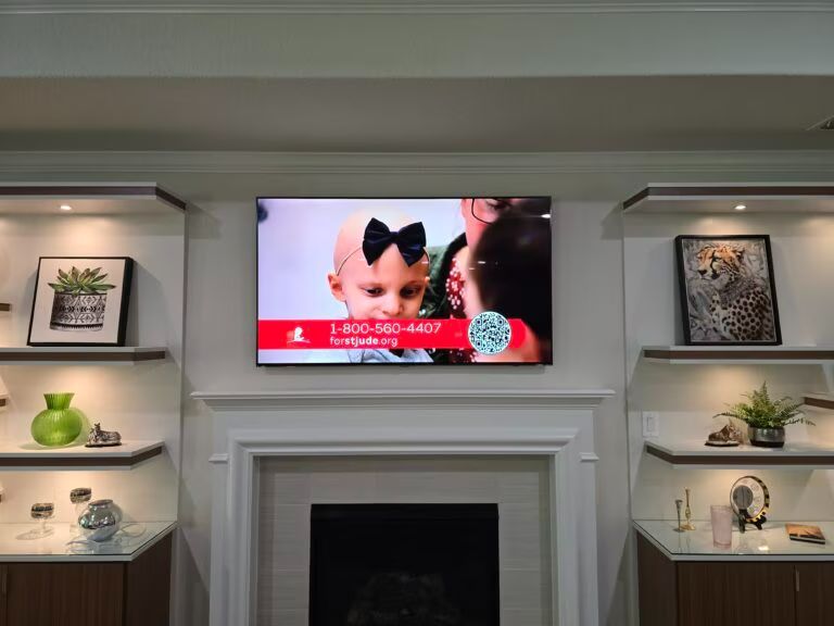 Living room with a TV above a fireplace, surrounded by shelves and decorative items