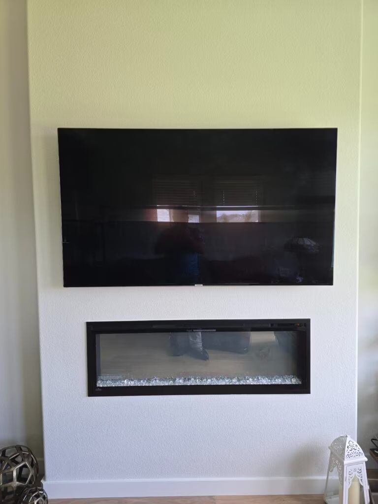 Black wall-mounted TV above a narrow glass fireplace on a white wall