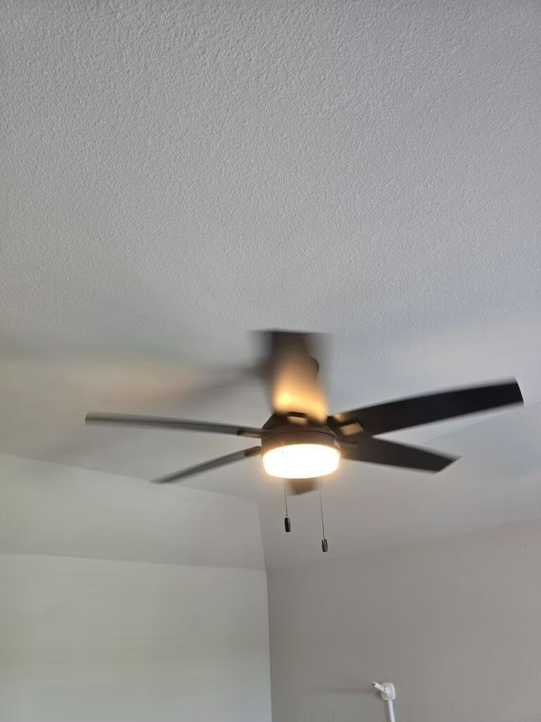 Ceiling fan with light on a textured white ceiling, viewed from below.