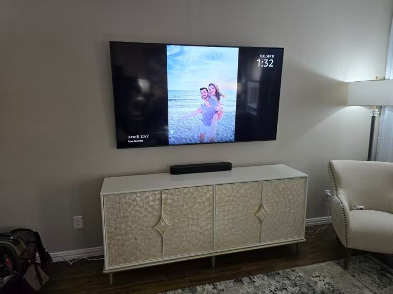 Living room wall-mounted TV above a white console, with a floor lamp and beige armchair nearby.