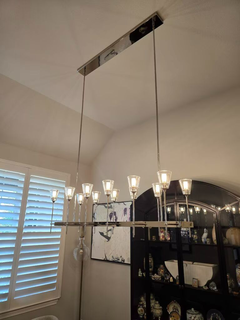 Dining chandelier hanging from ceiling with exposed wiring above a room with a window and mirror cabinet