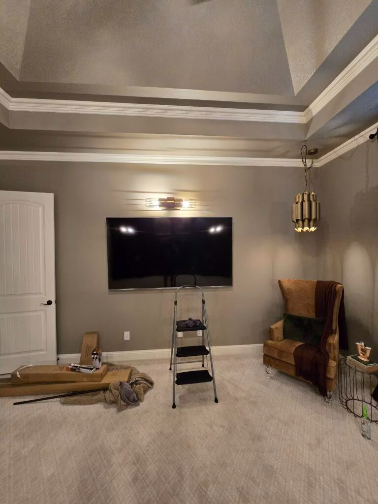 Living room with a wall-mounted TV, ladder, chair, boxes, and crown-molded ceiling.