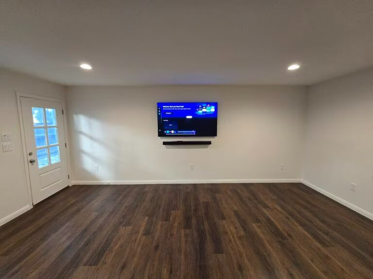 Empty living room with dark wood floors, white walls, and a wall-mounted TV.