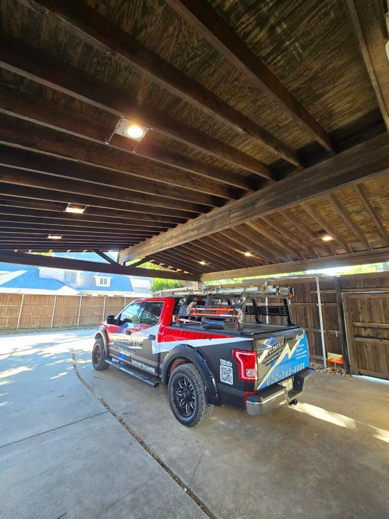 Red and blue pickup truck parked under a covered carport with exposed wooden beams.