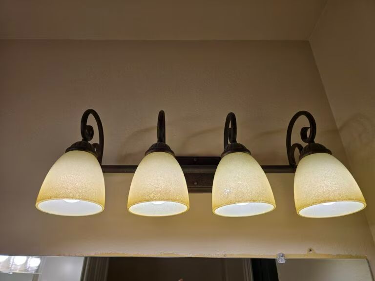 Four-bulb vanity light with frosted glass shades mounted on a bathroom wall.