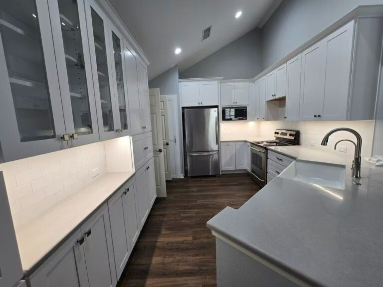 Modern white kitchen with stainless steel appliances, dark wood floor, and long countertop island