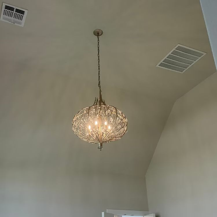 A hanging crystal chandelier glows in a white vaulted room with ceiling vents.