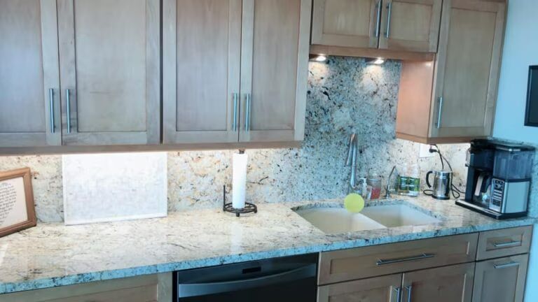Modern kitchen with wood cabinets, granite countertop, lit backsplash, sink, coffee maker, and dishwasher