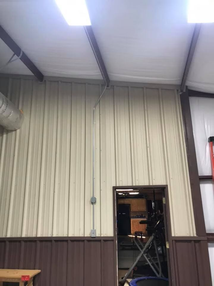 Interior of a metal building with high ceiling, fluorescent lights, and an open doorway to another room
