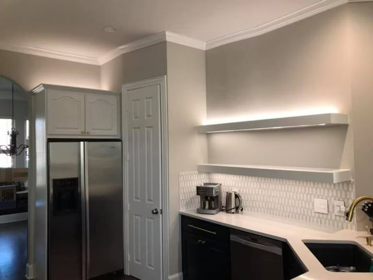 Modern kitchen with stainless steel fridge, gray cabinets, and black countertops with open shelves.