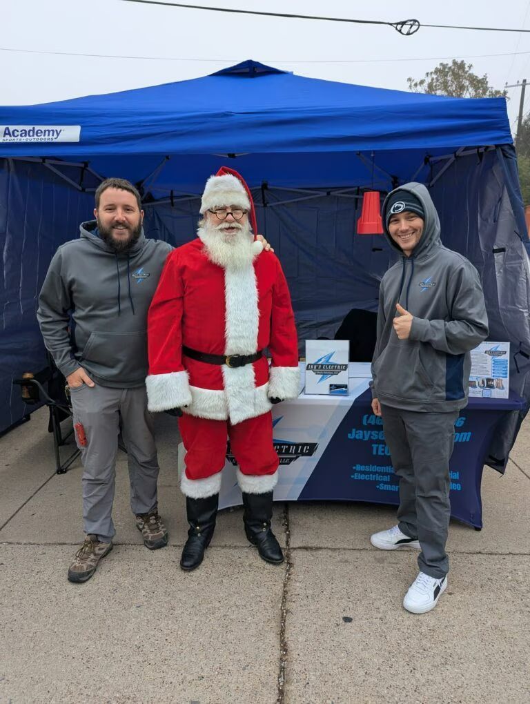 Three people pose by a blue tent, with Santa in the center giving a thumbs up.