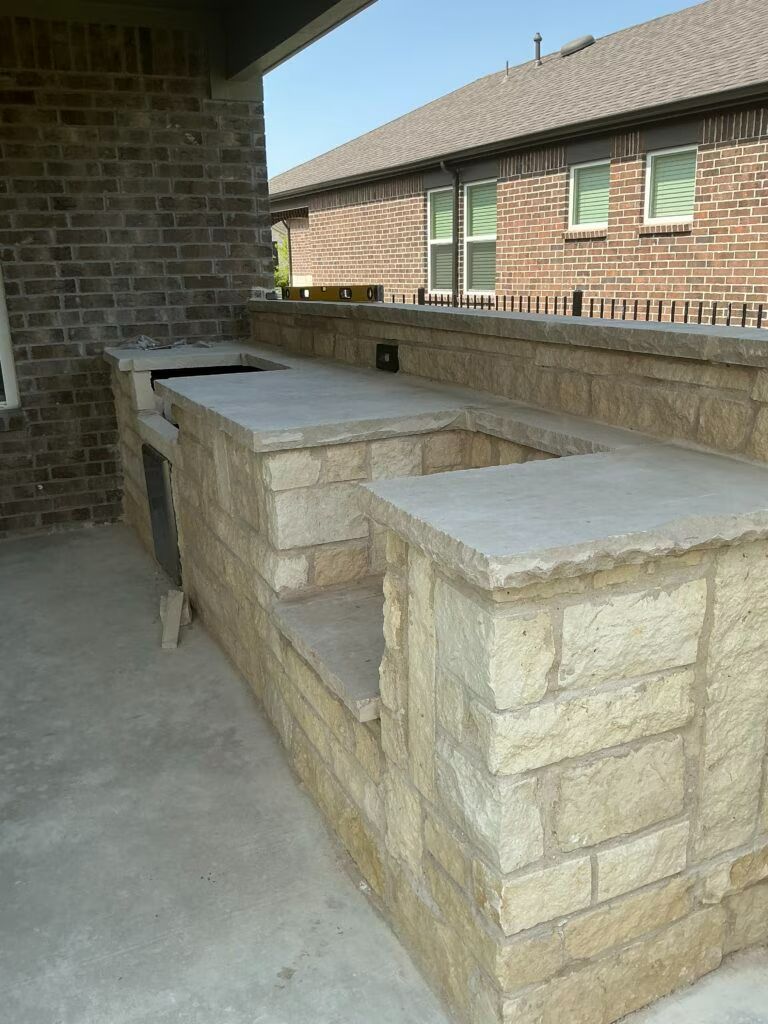 Stone outdoor kitchen or bench under a covered patio beside a brick house