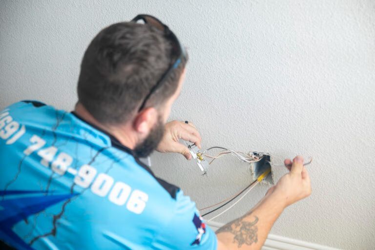 Technician in blue shirt wiring a wall outlet against a white wall