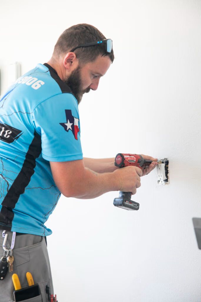 Worker drilling into a white wall with a power drill, wearing a blue shirt and tool belt.