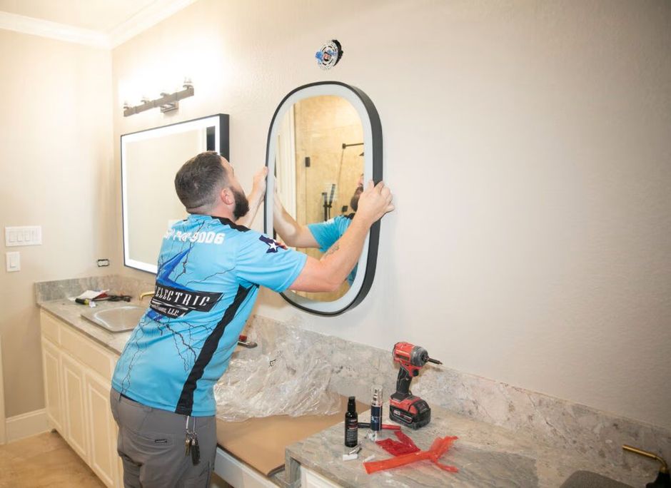 Technician installing a round mirror above a granite bathroom vanity with tools on the counter