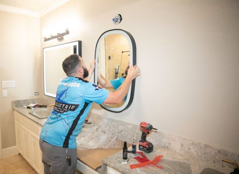 Man installing a bathroom mirror above a granite vanity with a drill and tools nearby
