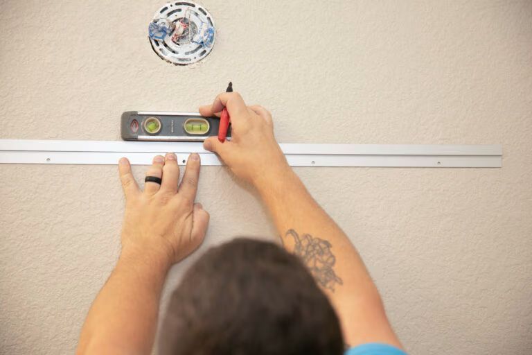 Person using a level to mark a line on a wall above a hanging plate measuring guide