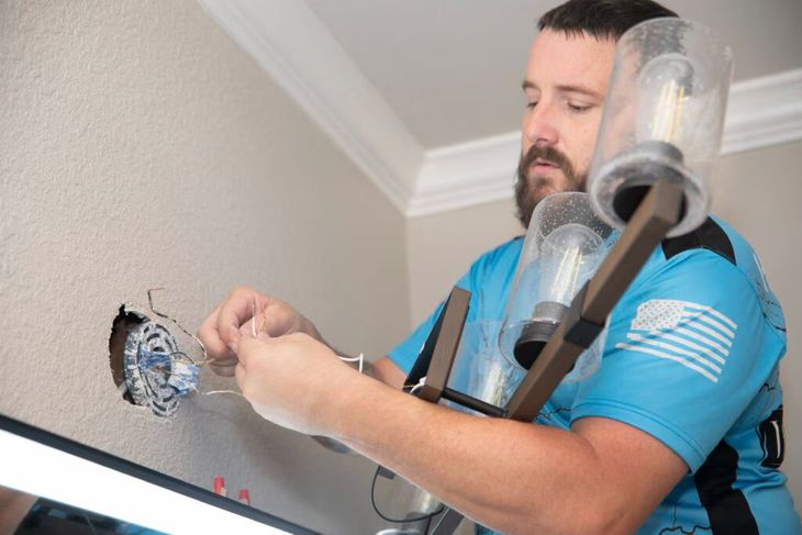 Technician using a tool to install or repair wiring near a ceiling fixture