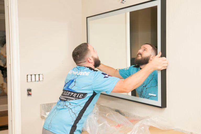 Man in blue shirt installing a wall mirror, reflected in the mirror during home interior work