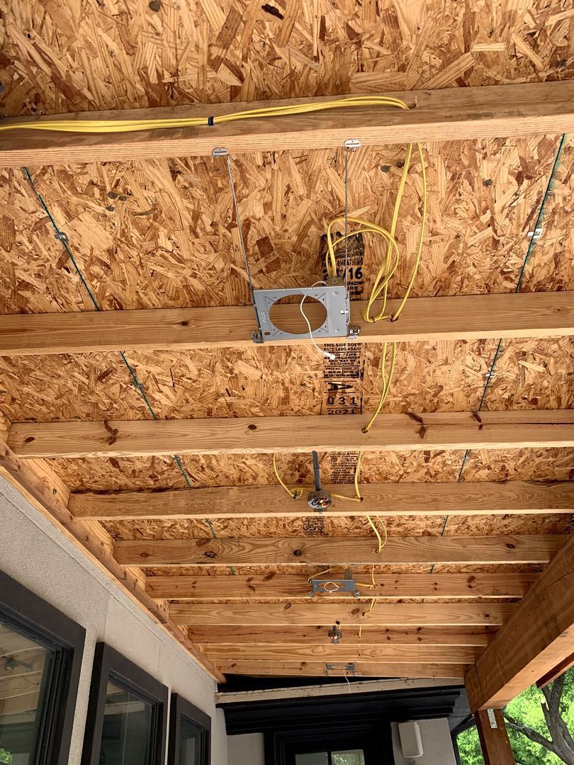 Unfinished porch ceiling with exposed wooden joists and hanging electrical wiring above a screened patio.