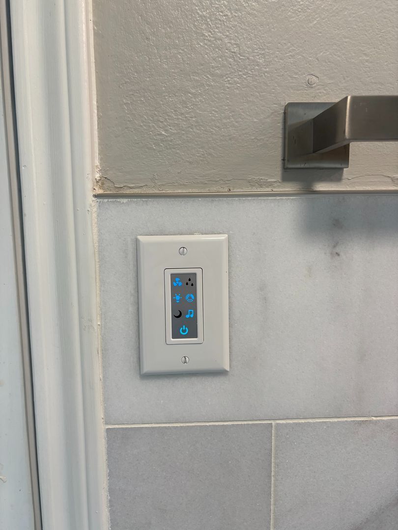 Wall-mounted touchscreen control panel beside a door on a tiled wall